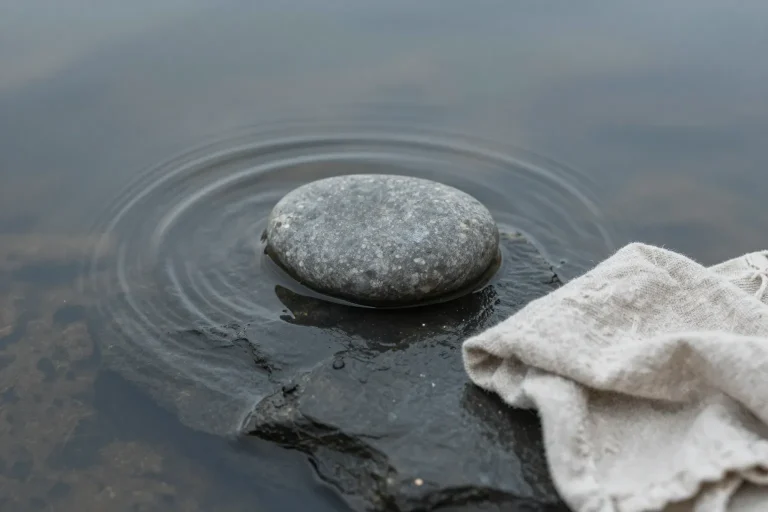 石頭落入淺水面盪出同心圓漣漪，旁邊放著一塊素麻布——比喻聲音（漣漪）被轉換成可以攤平閱讀的文字載體（布面）